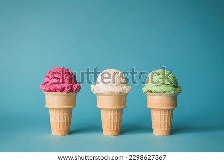 Three ice cream cones in a variety of flavours on blue background.
