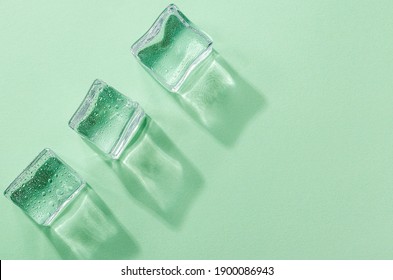 Three Ice cubes with reflexes on pastel green color background. Concept art. Minimal surrealism. Flat lay with copy space. Soft focus.