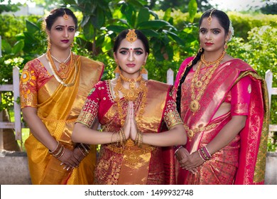 Three Indian lady in traditional South Indian bridal look in welcome expression, wearing sari and heavy gold jewelry