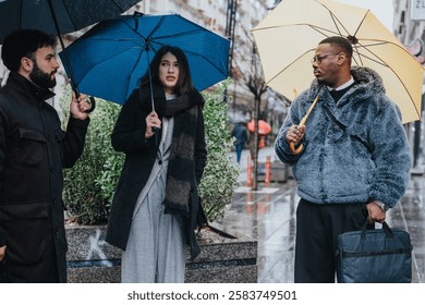 Three individuals having a collaborative conversation while standing outside on a rainy day, using umbrellas for cover.