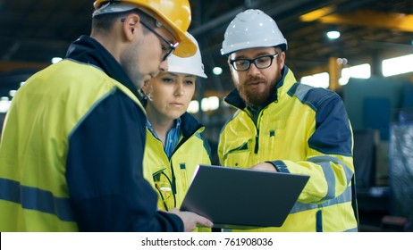 Three Industrial Engineers Talk with Factory Worker while Using Laptop. They Work at the Heavy Industry Manufacturing Facility.