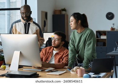 Three intercultural designers or programmers looking at new software product on computer screen in coworking space