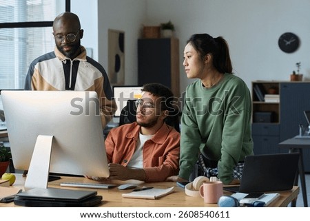 Three intercultural designers or programmers looking at new software product on computer screen in coworking space