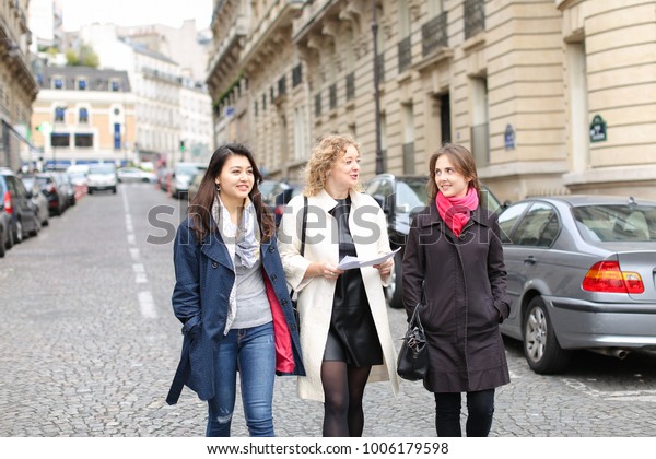 Three international students learning
English and passing in  . Concept of language courses and preparing
for lessons. Girls walking in city after
classes.