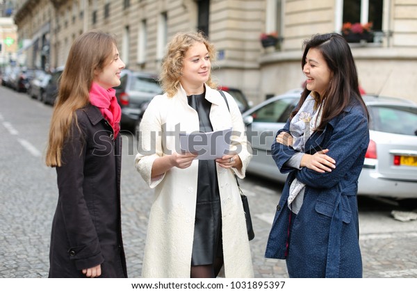 Three international students learning\
English and passing in  . Concept of language courses and preparing\
for lessons. Girls walking in city after\
classes.