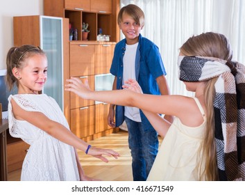 Three joyful kids playing with blindfold in the living room
