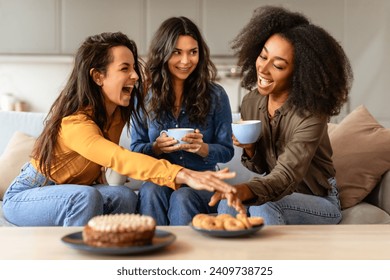 Three joyful multiethnic friends ladies share laughter and stories over cups of coffee and plate of cookies, creating warm, cozy atmosphere in stylish living room. Friendship concept - Powered by Shutterstock