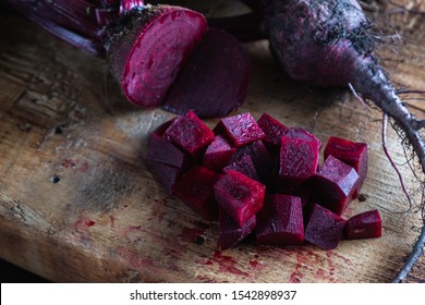 three juicy beets with leaves, one of which sliced lies next to diced beets on a wooden board. horizontal orientation. ugly food. dark background. - Powered by Shutterstock