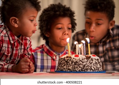 Three kids blowing candles out. Boys blow cake's candles out. Moment they've been waiting for. Important part of the tradition.