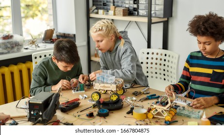 Three Kids Building Robots And Vehicles At Robotics Lesson. Smart Children And STEM Education. Science And People Concept. Horizontal Shot. Selective Focus