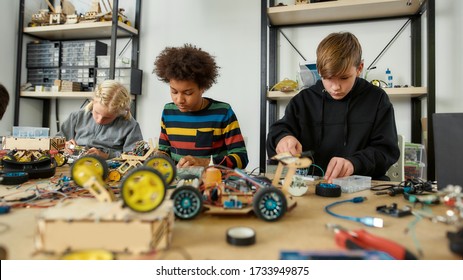 Three Kids Building Robots And Vehicles At Robotics Lesson. Smart Children And STEM Education. Science And People Concept. Horizontal Shot. Selective Focus