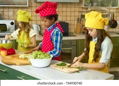 Three kids in the kitchen. Little girl cutting onion. Cooking classes for children.