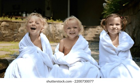 Three Kids Laugh Wrapped In A White Towel After Taking A Dip In The Pool While On Vacation. The Contagious Laughter Of Children Who Are Washed Away In The Frame. Vacation Concept With Children.