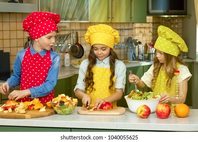 Three Kids Making Salad, Kitchen. Cut Fruits And Vegetables.