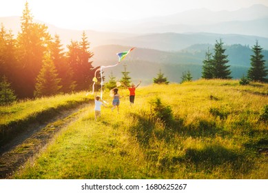 Three kids in the mountains at sunset play kite and butterfly fishing net. Happy summer holidays and childhood. Beautiful mountain landscape in summer in sunny weather.