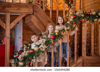 Three Kids On The New Year Decorated Stairs - Wooden House - Friends At Home Two Girls And Boy Ready For The Christmas 