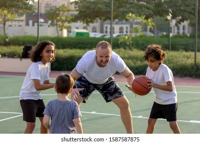 Three Kids Practice Basketball With  Trainer.Group Of Multiracial Young People Playing Basketball On Court.