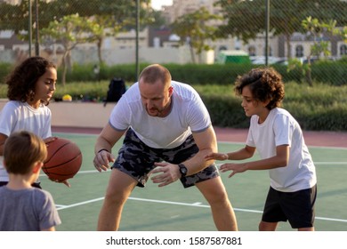 Three Kids Practice Basketball With  Trainer.Group Of Multiracial Young People Playing Basketball On Court.