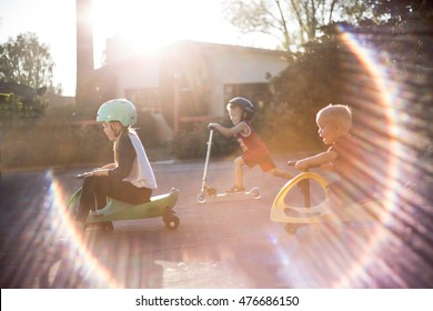 Three Kids Riding Scooters And Bikes With Sun Flare