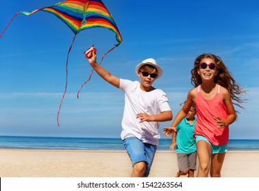 Three Kids Run On The Beach With Kite