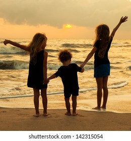 Three Kids Silhouettes Standing On Beach At Sunset