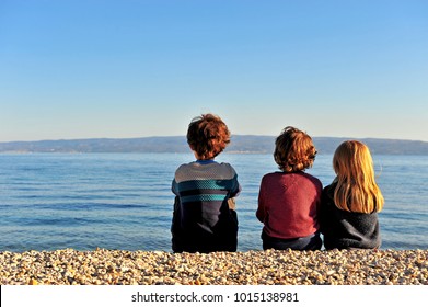 Three Kids Sitting On The Beach On Sunset