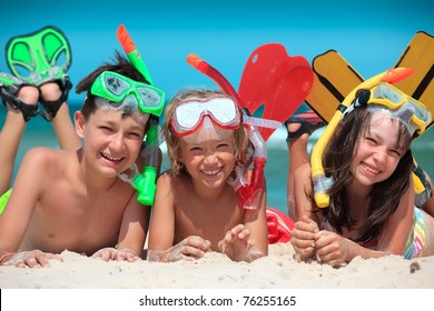 Three Kids With Snorkels And Fins On The Beach.