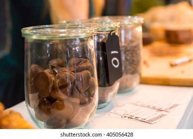 Three Large Glass Jars Of Chocolate Sweets For Sale On Counter With Tickets In Front Of Them At Cafe Or Store