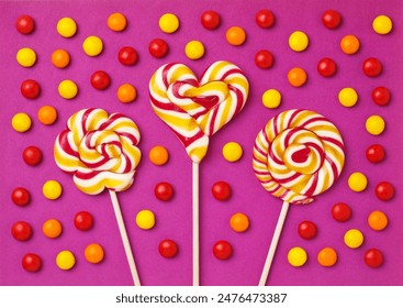 Three large lollipops on a stick in the shape of a circle, a flower and a heart surrounded by red and yellow candies on a purple background, handmade. close-up - Powered by Shutterstock