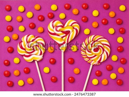 Three large lollipops on a stick in the shape of a circle, a flower and a heart surrounded by red and yellow candies on a purple background, handmade. close-up