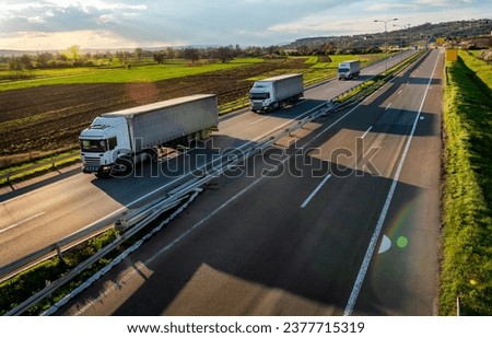 Three large Transportation Trucks on a highway road through the countryside under sunset sky