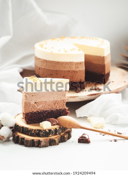 Three layered chocolate mousse\
cake on the wooden stand on white background. Good morning with\
fresh coffee and chocolate souffle cake. Vintage\
background