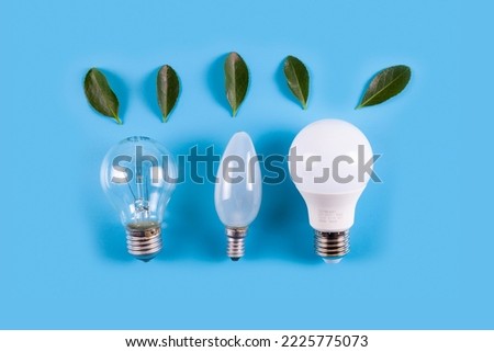 Three light bulbs with fresh green leaves on a blue background. Energy conservation, ecology and sustainable conservation of environmental resources. 