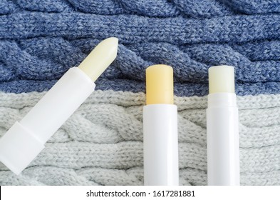 Three lip balms on the knitted background. Winter lip care sticks with beeswax, honey, panthenol and shea butter. Copy space. 