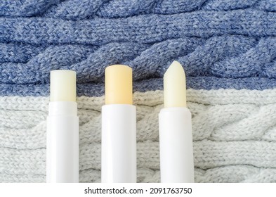 Three lip balms on a knitted background. Winter lip care sticks with beeswax, honey, panthenol and shea butter. Copy space.