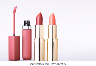 Three lipsticks against a white background, including a liquid lipstick with a pink applicator wand, and two lipsticks in gold cases, one in a vibrant red shade and the other in a soft coral shade.