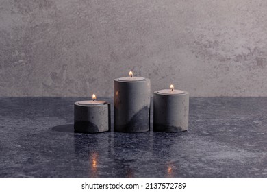 Three lit candles in concrete cement holder on grey texture background