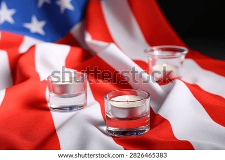 Three lit tea light candles in glass holders on a draped American flag, Memorial and remembrance