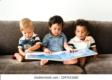 Three little boys reading a book on a sofa