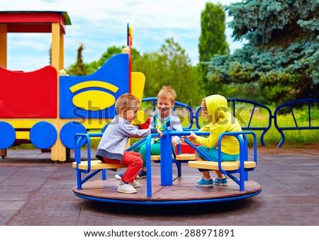 three little friends, kids having fun on roundabout at playground