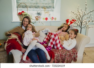 Three Little Girls Are Relaxing On The Sofa With Their Mother At Christmas Time, Watching The Television. 