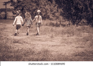Three Little Girls Walking Outdoors Holding Hands. Girlfriends Or Sisters. Childhood. Friendship. Kids Playing Outside Summer. Black And White Photo. Vintage. Retro