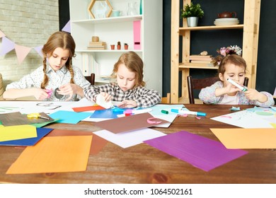 Three little sisters wrapped up in creating pictures from colored paper while gathered together at modern living room