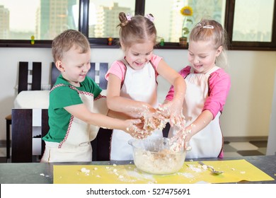 Three lovely children preparing a cake of dough in the kitchen. Healthy eating