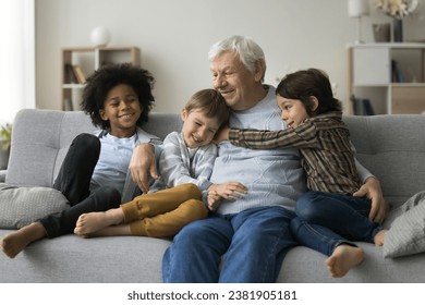 Three loving cute multiracial great-grandsons cuddling his grey-haired old great-grandpa express love and attachment sit together on couch enjoy time together at home. Multigenerational family ties - Powered by Shutterstock