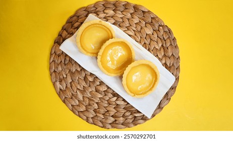 Three luscious egg tarts, goldenyellow and glistening, rest on a woven mat. A simple, yet elegant presentation, perfect for a sweet afternoon.