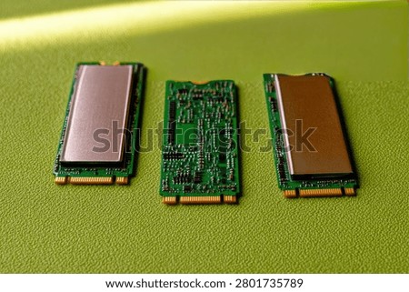 Three M.2 NVMe Solid State Drives are displayed on a vibrant green textured background. One SSD is shown with its cover removed, revealing the circuit board, while the other two are fully assembled.