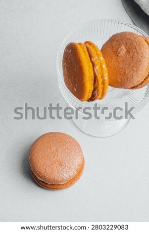 Three macarons sit on a white surface, two on a glass dish.
