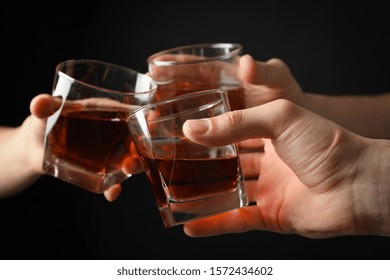 Three Male Hands Holds Glasses Of Whiskey On Black Background, Close Up. Cheers