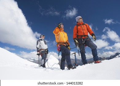 Three Male Mountain Climbers Reaching Snowy Peak Against Clouds